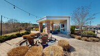 Located at 5437 Bowman Rd in Macon, Georgia, this outdoor amenity space is thoughtfully designed for relaxation and social gatherings. The centerpiece of the area is a covered pavilion supported by striking brick columns, featuring ceiling fans to ensure comfort during warmer months and a wall-mounted television for outdoor entertainment. Adjacent to the pavilion, a dedicated lounge area offers cushioned seating, ideal for casual gatherings. A gravel fire pit area surrounded by Adirondack chairs provides a welcoming spot for evening socializing under string lights that stretch across the space, adding a warm, festive ambiance. The herringbone-patterned brick paver walkways connect the various zones of the outdoor area seamlessly. Mature landscaping, including ornamental grasses and shrubs, frames the space and adds natural texture throughout. A black wrought-iron perimeter fence encloses the area while preserving unobstructed views of the adjacent pond and surrounding greenery. The open sky and abundant natural light enhance the airy, expansive feel of this well-appointed outdoor retreat, making it a versatile and inviting communal space in the heart of Macon, GA.