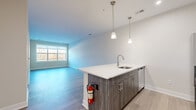 Located at 450 W Westfield Ave in Roselle Park, NJ, this well-designed one-bedroom, one-bathroom unit offers a modern living experience with thoughtful finishes throughout. The open-concept kitchen and living area serves as the heart of the home, anchored by a large central island with a crisp white quartz countertop, an undermount sink, and stylish pendant lighting overhead. The kitchen features dark wood-grain cabinetry, a white subway tile backsplash, and a full suite of stainless steel appliances including a refrigerator, range, and microwave. Light hardwood-style flooring flows throughout the main living area, complementing the clean, neutral color palette. A wide window in the living area allows natural light to fill the space and offers views of the surrounding landscape. The bedroom is a comfortable retreat finished with plush carpeting, warm neutral walls, and a large window framing outdoor greenery. It includes access to a dedicated closet, providing convenient storage. The bathroom is appointed with a dark wood-grain vanity, white quartz countertop, a large mirror, modern chrome fixtures, and a full soaking tub with shower. A hallway connects the spaces efficiently, completing this thoughtfully laid-out home.