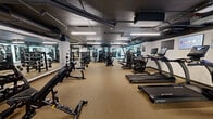 Located at 127 Northwest 27th Street in Miami's vibrant Wynwood neighborhood, this fitness facility offers a generously sized, single-floor exercise space designed to support a comprehensive range of workout routines. The floor plan follows an L-shaped layout, providing distinct zones for different training disciplines while maintaining an open, uncluttered feel throughout.

The exercise room features durable rubber flooring throughout, offering both comfort and safety for high-intensity training. The industrial-style ceiling exposes ductwork and structural elements painted in dark tones, lending the space a modern, urban aesthetic. Linear LED lighting runs across the ceiling, providing bright, even illumination across all workout areas.

The cardio zone houses a lineup of True-brand treadmills, stationary bikes, and rowing machines, complemented by mounted screens for entertainment and motivation. The strength training area is well-appointed with Hoist cable machines, weight benches, and a full rack of free weights with floor-to-ceiling mirrors along the walls, maximizing both functionality and spatial perception.

A dedicated functional training section features a turf sled track, resistance sleds, and open floor space for dynamic movement exercises. Additional amenities include a water fountain station. The facility is organized to accommodate multiple users simultaneously, making it a well-rounded, professionally equipped fitness destination.