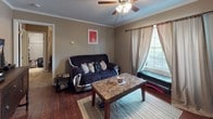 This single-floor residence offers a practical and efficiently organized layout within a compact footprint. The living area serves as the central hub of the home, featuring rich hardwood-style flooring, crown molding, and a ceiling fan that provides both lighting and air circulation. A window dressed with layered curtains allows natural light to filter into the space while offering privacy. The living area comfortably accommodates a seating arrangement alongside a dining area, making it a versatile space for both relaxing and entertaining.

The galley-style kitchen is thoughtfully arranged to make efficient use of its narrow footprint, equipped with white cabinetry, countertop workspace, a dishwasher, and a full-size refrigerator. The wood-look flooring continues throughout, maintaining a cohesive aesthetic.

The bathroom features the same wood-look flooring, a dark-toned vanity with a framed mirror, and a shower-tub combination with a striped curtain, lending the space a clean, functional character.

Overall, the residence is designed with practicality in mind, offering consistent flooring, crown molding details, and natural light throughout its well-connected rooms.
