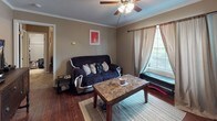 This single-floor residence offers a practical and efficiently organized layout within a compact footprint. The living area serves as the central hub of the home, featuring rich hardwood-style flooring, crown molding, and a ceiling fan that provides both lighting and air circulation. A window dressed with layered curtains allows natural light to filter into the space while offering privacy. The living area comfortably accommodates a seating arrangement alongside a dining area, making it a versatile space for both relaxing and entertaining.

The galley-style kitchen is thoughtfully arranged to make efficient use of its narrow footprint, equipped with white cabinetry, countertop workspace, a dishwasher, and a full-size refrigerator. The wood-look flooring continues throughout, maintaining a cohesive aesthetic.

The bathroom features the same wood-look flooring, a dark-toned vanity with a framed mirror, and a shower-tub combination with a striped curtain, lending the space a clean, functional character.

Overall, the residence is designed with practicality in mind, offering consistent flooring, crown molding details, and natural light throughout its well-connected rooms.