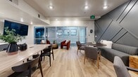 Located at 1001 Ross Ave in Dallas, Texas, this thoughtfully designed dining space offers a refined and contemporary atmosphere across a single floor. The room is anchored by a bold geometric accent wall finished in deep charcoal gray, featuring angular paneling that adds dramatic visual depth to the space. Light hardwood flooring runs throughout, providing a warm contrast to the darker design elements.

The dining area is divided into distinct seating zones, offering versatility for various group sizes. A large rectangular light-wood dining table with stylish dark chairs serves as the central gathering point, complemented by a built-in credenza finished in muted gray cabinetry. Elegant brass pendant lights hang above the credenza alongside a wall-mounted flat-screen display, enhancing the functionality of the space.

A cozy banquette seating nook features channel-tufted upholstered benches paired with a round bronze-toned table and upholstered armchairs, creating an intimate dining experience. Glass partition walls allow natural light to flow in from an adjacent outdoor area, contributing to the open and airy feel of the room. Recessed ceiling lighting throughout ensures well-distributed illumination, while carefully placed greenery adds a refreshing organic touch to the polished, modern aesthetic.