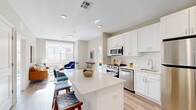 Located at 30 W Broad St, this thoughtfully designed one-bedroom, two-bathroom residence offers a functional and stylish single-floor layout. The open-concept kitchen is a standout feature, equipped with stainless steel appliances, white shaker cabinetry, a classic subway tile backsplash, and a quartz-topped center island with bar seating — seamlessly connecting to the living and dining areas. Light hardwood-style flooring runs throughout, complementing the neutral, modern palette.

The living room benefits from oversized windows that invite abundant natural light and offer views of the surrounding streetscape. A dedicated office space, also bathed in natural light from large windows, provides a versatile area suitable for work or additional living use.

The primary bedroom features expansive corner windows with urban views, creating a bright and airy retreat. Both bathrooms are finished with neutral tile flooring, white vanities with under-cabinet storage, and clean, contemporary fixtures — one including a glass-enclosed shower.

A connecting hallway provides practical flow between the private and shared spaces of the residence. Throughout, the design emphasizes clean lines, consistent finishes, and a bright, welcoming ambiance well-suited for modern urban living.