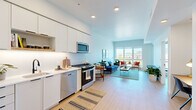 This thoughtfully designed one-bedroom, one-bathroom residence offers a efficient and functional single-floor layout with a bright, contemporary aesthetic throughout. The open-concept living and kitchen area creates a seamless flow, anchored by light hardwood flooring and crisp white walls that reflect abundant natural light. Soaring ceilings in the main living area enhance the sense of spaciousness, while large floor-to-ceiling windows and a sliding glass door frame sweeping city and skyline views, filling the space with sunlight.

The kitchen is outfitted with sleek white flat-front cabinetry extending to the ceiling, white quartz countertops, under-cabinet lighting, and a full suite of stainless steel appliances including a gas range, dishwasher, microwave, and refrigerator. The living room offers generous space for entertaining, with direct access to an outdoor balcony through the sliding glass door.

The bedroom is a serene retreat with its own balcony access and expansive windows showcasing panoramic city views. The bathroom features classic white square tile surrounding a full soaking tub with shower, complemented by matte black fixtures. A dedicated in-unit laundry closet houses a stacked full-size washer and dryer. An additional closet provides practical storage, completing this well-appointed urban residence.