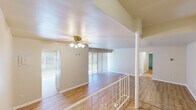 This single-floor space is characterized by a thoughtful split-level layout, with distinct areas connected by a short staircase and an ornamental white railing with a decorative column — an architectural detail that adds visual interest while defining separate living zones. Light wood laminate flooring runs consistently throughout, lending warmth and continuity across the space.

The main living area is generously proportioned, featuring a ceiling fan with integrated lighting and large sliding glass doors dressed with vertical blinds, allowing natural light to filter in. A second living or dining area benefits from additional sliding glass door access, further enhancing the brightness of the space.

The kitchen is equipped with light wood cabinetry, a gas range, a dishwasher, and a double sink, alongside a sliding window that introduces natural light and ventilation. The layout is functional and well-organized.

The bedrooms are spacious, each offering notable closet space, including walk-in closets with built-in shelving. The two bathrooms are clean and practical — one features a full tub-shower combination with white tile surround, while the other includes a wood-toned vanity with a speckled countertop and framed mirrors. Neutral tones throughout create a calm, cohesive ambiance.