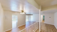 This single-floor space is characterized by a thoughtful split-level layout, with distinct areas connected by a short staircase and an ornamental white railing with a decorative column — an architectural detail that adds visual interest while defining separate living zones. Light wood laminate flooring runs consistently throughout, lending warmth and continuity across the space.

The main living area is generously proportioned, featuring a ceiling fan with integrated lighting and large sliding glass doors dressed with vertical blinds, allowing natural light to filter in. A second living or dining area benefits from additional sliding glass door access, further enhancing the brightness of the space.

The kitchen is equipped with light wood cabinetry, a gas range, a dishwasher, and a double sink, alongside a sliding window that introduces natural light and ventilation. The layout is functional and well-organized.

The bedrooms are spacious, each offering notable closet space, including walk-in closets with built-in shelving. The two bathrooms are clean and practical — one features a full tub-shower combination with white tile surround, while the other includes a wood-toned vanity with a speckled countertop and framed mirrors. Neutral tones throughout create a calm, cohesive ambiance.