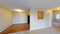 This single-floor unit offers a practical and functional layout with a comfortable mix of flooring materials and neutral tones throughout. The living and dining area is a generous, open space with warm hardwood-style flooring, a baseboard heating system, and a ceiling-mounted light fixture. A half-wall partition separates this area from the kitchen, featuring a convenient pass-through window that maintains an open, connected feel between the two spaces.

The kitchen is equipped with black appliances, including a refrigerator, range, and dishwasher, complemented by honey-toned wood cabinetry and granite-style countertops. Hardwood-style flooring continues throughout the kitchen, adding warmth and cohesion.

The bedrooms are carpeted and finished with neutral beige walls. One bedroom includes a sliding closet with a clothing rod, providing practical storage. Windows fitted with blinds allow natural light to filter into the rooms. A textured ceiling adds subtle visual interest.

The bathroom features a single-sink vanity with a wood-framed mirror, a tub-shower combination, and tile flooring in a stone-like pattern.

The living area opens via a sliding glass door to a private balcony, offering outdoor views and natural light. Baseboard heaters and a wall-mounted air conditioning unit provide year-round climate control.