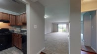 Located at 5 Stonewain Court in Towson, Maryland, this single-floor residence offers a thoughtfully laid-out floor plan with a clean, neutral aesthetic throughout. The open living area is generously proportioned, featuring wall-to-wall carpeting and a large sliding glass door that fills the space with natural light and provides views of the surrounding greenery. The seamless flow between the living area and the rest of the home creates a comfortable, functional environment. The kitchen is well-appointed with rich wood cabinetry, dark granite-style countertops, black appliances including a gas range and refrigerator, and durable wood-look vinyl flooring — offering both practicality and visual appeal. The bedrooms are carpeted and offer a calm, neutral palette, with one room featuring a distinctive teal accent wall that adds a pop of color. The layout, as visible in the overhead dollhouse view, reflects an efficient use of space with clearly defined areas for living, cooking, and sleeping. Throughout the home, white trim and soft neutral wall tones contribute to a bright, cohesive interior. The combination of natural light, functional design, and comfortable finishes makes this Towson residence a practical and inviting home.