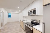 Located at 139 S Occidental Blvd in Los Angeles, CA, this thoughtfully designed one-bedroom, one-bathroom unit offers a clean, contemporary aesthetic throughout its efficiently utilized single floor. The open kitchen serves as the heart of the space, boasting floor-to-ceiling white cabinetry, warm wood-toned lower cabinets, white quartz countertops, and a full suite of stainless steel appliances including a refrigerator, electric range, dishwasher, and over-the-range microwave. Light hardwood-style flooring runs through the kitchen and main living area, contributing to a bright, airy feel complemented by recessed lighting. The bedroom features soft neutral carpeting, a window that brings in natural light, and a built-in closet for organized storage. An additional shelved closet in the bedroom hallway provides further storage flexibility. The bathroom maintains the same modern design language, featuring a wood-grain vanity with white quartz countertop, an undermount sink, and a large wall mirror. A clean entry corridor connects all rooms cohesively. The overall design is minimalist and functional, with a consistent white-and-wood palette that creates a calm, modern living environment well-suited for urban life in Los Angeles.