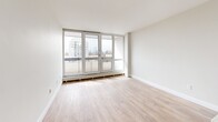 Located at 221 Balliol St in Toronto's vibrant Davisville Village neighbourhood, this well-appointed one-bedroom, one-bathroom unit offers a thoughtfully designed open-concept layout across a single floor. Light hardwood flooring flows throughout the main living areas, complementing the bright, neutral palette that defines the space.

The combined kitchen and living room serves as the heart of the unit. The kitchen is outfitted with sleek, high-gloss white upper cabinetry, contrasting grey lower cabinets, light stone countertops, a peninsula island ideal for casual dining, and stainless steel appliances including a refrigerator and range. The adjacent living area is bathed in natural light, courtesy of expansive floor-to-ceiling windows and French doors that open onto a balcony with open city views.

The bedroom is a quiet, well-proportioned room featuring the same warm hardwood flooring, large windows with balcony access, and a double-door closet offering ample storage. The bathroom is finished with crisp white subway tile surrounding a full soaker tub and shower combination, paired with chrome fixtures for a clean, modern look. A hallway with recessed lighting connects all areas efficiently, completing this functional and contemporary urban residence.