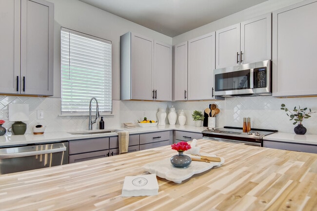Cocina contemporánea con isla grande, fregadero estilo granja, lavavajillas de acero inoxidable y salpicadero de azulejos tipo metro. - Legacy Farms