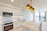 Located at 1532 S Federal Hwy in Boynton Beach, Florida, this well-appointed one-bedroom, one-bathroom residence offers a thoughtfully designed single-floor layout with a clean, modern aesthetic throughout. Light wood-style flooring flows through the open-plan living and kitchen areas, creating a bright and cohesive feel.

The kitchen is a standout feature, showcasing crisp white shaker cabinetry adorned with gold hardware, a classic subway tile backsplash, stainless steel appliances including a double oven and built-in microwave, and a generously sized waterfall quartz island. A trio of gold pendant lights adds warmth and sophistication to the space.

The living room opens directly to a private balcony through floor-to-ceiling sliding glass doors, flooding the room with natural light and offering scenic treetop views. A ceiling fan enhances comfort throughout.

The spacious primary bedroom features plush carpeting, a ceiling fan, and a large window with lush outdoor views. An adjacent walk-in closet with wire shelving provides ample storage. The bathroom continues the gold-accent theme with a wide vanity, gold fixtures, and a well-lit mirror. A stacked in-unit washer and dryer is conveniently tucked near the entryway hallway, adding everyday practicality to this polished Boynton Beach residence.