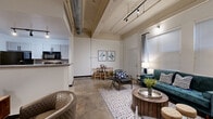 Located at 3201 First Ave in Columbus, GA, this one-bedroom, one-bathroom loft showcases a distinctive industrial-chic aesthetic that blends raw architectural character with modern finishes. Soaring ceilings with exposed ductwork, structural beams, and track lighting set the tone throughout the open-concept main living area. Polished concrete floors run seamlessly across the space, reinforcing the loft's urban character.

The combined living and dining area is generously proportioned, offering room for multiple seating arrangements and a dining set, all bathed in natural light from large windows dressed with blinds and draping curtains. A peninsula-style kitchen features white shaker cabinetry, a breakfast bar, and black appliances, with an adjacent pantry providing additional storage.

The bedroom is a serene retreat, featuring soaring ceilings with exposed beams, floor-to-ceiling draping curtains, and ample natural light. A dedicated closet offers practical built-in wire shelving for organized storage.

The bathroom is clean and well-appointed, with a single vanity, large mirror, modern matte-black fixtures, and a stacked in-unit washer and dryer tucked neatly behind louvered doors. Every detail of this space reflects a cohesive urban loft sensibility with comfortable, functional living in mind.