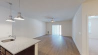 This single-floor residence is designed with a clean, contemporary aesthetic and a practical open-concept layout. The kitchen serves as a central hub, outfitted with rich dark cabinetry, stainless steel appliances including a refrigerator, range, and microwave, and a granite-topped peninsula with an undermount sink. Pendant lighting illuminates the peninsula, adding a polished finish to the space. Light wood-tone flooring flows throughout the kitchen and living areas, enhancing the sense of openness and continuity.

The living area is generously proportioned, featuring a ceiling fan and a sliding glass door with vertical blinds that provides access to an outdoor area and brings in natural light. An in-unit laundry area is conveniently accessible from the main living space.

The bedrooms are carpeted for comfort. The primary bedroom connects to a walk-in closet outfitted with wire shelving and an en-suite bathroom featuring a white step-in shower with chrome fixtures. A secondary bedroom offers a window with natural views and ample space. The overall palette of crisp white walls and neutral tones creates a bright, welcoming atmosphere throughout.