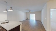 This single-floor residence is designed with a clean, contemporary aesthetic and a practical open-concept layout. The kitchen serves as a central hub, outfitted with rich dark cabinetry, stainless steel appliances including a refrigerator, range, and microwave, and a granite-topped peninsula with an undermount sink. Pendant lighting illuminates the peninsula, adding a polished finish to the space. Light wood-tone flooring flows throughout the kitchen and living areas, enhancing the sense of openness and continuity.

The living area is generously proportioned, featuring a ceiling fan and a sliding glass door with vertical blinds that provides access to an outdoor area and brings in natural light. An in-unit laundry area is conveniently accessible from the main living space.

The bedrooms are carpeted for comfort. The primary bedroom connects to a walk-in closet outfitted with wire shelving and an en-suite bathroom featuring a white step-in shower with chrome fixtures. A secondary bedroom offers a window with natural views and ample space. The overall palette of crisp white walls and neutral tones creates a bright, welcoming atmosphere throughout.