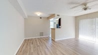 This single-floor residence offers a functional and comfortable layout with consistent finishes throughout. The open living area is finished with light-toned laminate wood flooring, neutral beige walls, and a textured ceiling. A ceiling fan provides year-round comfort, while a large sliding glass door fitted with vertical blinds fills the space with natural light and provides outdoor access. A pass-through kitchen bar connects the living area to the kitchen, which features dark espresso cabinetry, light countertops, a stone tile backsplash, and a full suite of black appliances including a refrigerator, range, dishwasher, and over-the-range microwave. The kitchen is finished with tile flooring and includes a window for additional natural light. An in-unit washer and dryer area is conveniently located adjacent to the kitchen. The bedrooms continue the laminate wood flooring and neutral color palette, each equipped with ceiling fans and closet storage. One bedroom features a double sliding-door closet with built-in shelving, while another benefits from a bright window with vertical blinds. The bathroom includes a tub-shower combination, a vanity with dark cabinetry, and tile flooring, maintaining a clean and cohesive aesthetic throughout the home.
