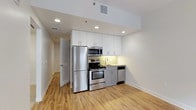 This single-floor unit presents a clean, modern design throughout its well-organized layout. The open kitchen is equipped with a full suite of stainless steel appliances, including a range with oven, built-in microwave, refrigerator, and dishwasher. White upper cabinetry pairs with light gray lower cabinets, complemented by a yellow-green subway tile backsplash and recessed lighting overhead. Light wood-look flooring extends through the main living and kitchen areas, adding warmth to the neutral color palette.

The living area is open and bright, benefiting from recessed lighting and a clean, minimalist aesthetic. The bedrooms feature plush carpeting and are well-lit by multiple windows with blinds, allowing for ample natural light. A sliding barn-style door adds a practical design touch to one bedroom. Both bedrooms offer comfortable proportions and easy access to the rest of the unit.

Storage is addressed through a dedicated walk-in closet fitted with dual hanging rods and wood flooring. The bathroom features neutral tile flooring, a walk-in shower enclosed by glass and finished with white subway tile, and chrome fixtures throughout. An in-unit washer and dryer is also included, adding everyday convenience to this thoughtfully designed space.