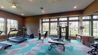 This fitness center in Panama City Beach, Florida, offers a thoughtfully designed, single-floor facility built to support a comprehensive workout experience. The space is anchored by a striking geometric-patterned carpet in shades of teal, gray, and white, adding a modern, energetic aesthetic that complements the warm brown-toned walls throughout.

Large multi-pane windows line multiple walls, flooding the interior with natural light and providing pleasant views of the surrounding greenery. Recessed ceiling lighting supplements the natural light, ensuring the space remains bright and functional at all hours.

The cardio zone is well-appointed with treadmills, elliptical trainers, and a stationary bike, each positioned to take advantage of the outdoor views. The strength training area includes a multi-station cable machine, adjustable benches, and a full rack of dumbbells, catering to a wide range of fitness routines. A full-length mirror wall visually expands the space and aids in form correction during workouts. Stability balls and additional accessories round out the available equipment.

A separate children's area provides a cozy, dedicated nook featuring a wall-mounted television, a small activity table, educational toys, and storage shelving, making the facility family-friendly and accommodating for all visitors.