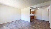 This single-story unit offers a practical and well-organized layout designed for comfortable everyday living. The open living area is bright and airy, featuring neutral walls, wood-look laminate flooring, a textured ceiling, and a ceiling-mounted HVAC vent for efficient climate control. A large window dressed with vertical blinds allows natural light to fill the space, creating a welcoming atmosphere.

The galley-style kitchen is efficiently designed with abundant warm-toned wood cabinetry lining both sides, providing generous upper and lower storage. It is equipped with a white electric range, refrigerator, and a stainless steel sink with a window at the far end that brings in additional natural light. The countertops offer ample workspace, and the continuous wood-look flooring ties the kitchen seamlessly to the rest of the unit.

The bedroom is a comfortable, well-proportioned room with large windows featuring vertical blinds, providing both natural light and privacy. The space includes the same consistent flooring and neutral wall tones found throughout the unit.

The bathroom is clean and functional, featuring a wood-cabinet vanity with a countertop sink, a large mirror with overhead lighting, and a toilet. The flooring continues the cohesive wood-look style seen throughout the space. A dedicated entryway with a full-panel door completes this practical single-floor layout.