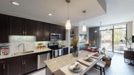Located in the desirable 77024 zip code of Houston, TX, this single-floor residence showcases a thoughtfully designed open-concept layout that seamlessly connects the kitchen, dining, and living areas. The kitchen is a standout feature, outfitted with rich dark espresso cabinetry extending to the ceiling, a light granite countertop island with bar seating, and a coordinating mosaic tile backsplash. Stainless steel appliances — including a refrigerator with ice and water dispenser, electric range, built-in microwave, and dishwasher — complete the well-appointed culinary space. Elegant pendant lighting hangs above the island, adding warmth and definition to the area. Hardwood-style flooring flows through the main living spaces, while recessed lighting keeps the interior bright and welcoming. The living area transitions smoothly toward a glass door that opens to an outdoor balcony, inviting natural light and neighborhood views. The bedroom is a serene retreat, featuring large windows overlooking lush greenery and a textured accent wall for added visual interest. The en-suite bathroom offers a dual-sink vanity with granite counters, dark cabinetry, a walk-in tiled shower, and direct access to the bedroom, creating a private, spa-like atmosphere.