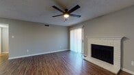 This single-story space is designed with a practical, cohesive layout that flows naturally from room to room. The living area serves as the focal point of the unit, anchored by a brick fireplace with a classic white surround and a sliding glass door fitted with vertical blinds, allowing natural light to filter in while providing outdoor access. Dark wood-look flooring runs consistently throughout, offering visual continuity and easy maintenance. A ceiling fan with integrated lighting is centrally positioned above, contributing to both comfort and functionality.

Adjacent to the living area, the open entry zone features two interior doors and additional ceiling fan lighting, connecting seamlessly to the rest of the home. The kitchen is well-equipped with ample white cabinetry, gray laminate countertops, a double basin sink, a dishwasher, and an electric range. A louvered bi-fold door opens to a dedicated pantry or utility closet, adding practical storage within the kitchen space.

The bedroom is a well-proportioned room with a ceiling fan, neutral gray walls, and a window that brings in natural light. The bathroom includes a clean, white tub-shower combination with a full surround and chrome fixtures. Textured ceilings and consistent neutral-toned walls throughout give the space a uniform, move-in-ready appearance.
