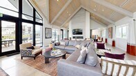 Located at 5400 Fowler Lane in Bozeman, Montana, this single-floor community space delivers an impressive blend of modern farmhouse architecture and contemporary interior design. The centerpiece of the space is a grand living room anchored by dramatic vaulted ceilings clad in warm wood planking, supported by exposed beams that draw the eye upward and create a sense of generous volume throughout. Floor-to-ceiling windows with sleek black framing flood the interior with natural light while offering views of the surrounding Bozeman landscape, including mountain vistas in the distance.

The lounge area is thoughtfully appointed with large sectional sofas, layered area rugs, and an assortment of seating arrangements that accommodate both social gatherings and quiet relaxation. A linear fireplace set into a shiplap accent wall serves as a focal point, complemented by a wall-mounted display above. Polished concrete flooring runs seamlessly throughout, adding an understated industrial touch that balances the warmth of the wood ceiling.

A well-equipped kitchenette features light wood cabinetry, a white quartz countertop, a teal tile backsplash, and built-in appliances, making it ideal for community use. Adjacent to the main lounge, glass-enclosed private work pods and a corridor of office spaces provide functional, quiet zones for focused work or meetings.