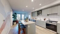 Located at 12520 Camino Del Sur in San Diego, CA, this well-appointed three-bedroom, two-bathroom residence offers a thoughtfully designed single-floor layout. The open-concept kitchen is a standout feature, showcasing sage-green flat-front cabinetry, a white subway tile backsplash, stainless steel appliances, and a central island with bar seating — seamlessly connecting to the living room. The living room is bright and welcoming, with large windows and a glass door that open onto a private balcony, flooding the space with natural light and outdoor views. Light wood-tone flooring flows consistently throughout, enhancing the airy, cohesive feel. The primary bedroom is a comfortable retreat, featuring soft blue-grey walls, a large window with sheer curtains, and generous closet space with built-in shelving and hanging rods. The additional bedrooms offer similar comfort and storage. Both bathrooms are clean and modern, with one featuring a full soaking tub and shower combo with white tile surround. A dedicated in-unit laundry room with stacked washer and dryer adds everyday convenience. A connecting hallway ties all rooms together efficiently, completing this well-organized and stylish San Diego residence.