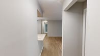 This single-floor, 3-bedroom, 2-bathroom residence offers a thoughtfully designed layout that maximizes functionality and comfort. The living room serves as the heart of the home, featuring warm wood-look luxury vinyl flooring and a large sliding glass door fitted with vertical blinds that floods the space with natural light. Neutral gray walls throughout create a clean, cohesive aesthetic.

The galley-style kitchen is well-equipped with crisp white shaker cabinetry, brushed nickel hardware, white quartz countertops, a subway tile backsplash, and stainless steel appliances. A dedicated laundry room is conveniently accessible directly from the kitchen and houses a full-size washer and dryer.

The three bedrooms are carpeted for comfort, each featuring neutral tones and ample natural light from large windows with blinds. The primary bedroom offers generous proportions and includes a closet with built-in shelving. Two closets throughout the unit provide additional storage. The two bathrooms are finished with wood-look flooring, white vanities with light countertops, and brushed nickel fixtures. Two hallways connect the living areas to the private bedroom wing, ensuring a smooth and practical flow throughout the residence.