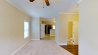 Located at 3304 Green Valley Rd in Fayetteville, North Carolina, this two-story home offers a practical and comfortable layout designed for everyday living. The main level features an open living area finished with plush carpeting and crown molding that adds a clean, classic detail to the space. A ceiling fan overhead provides both comfort and a functional accent to the room. Natural light filters in through a window, keeping the space bright and welcoming. The living area flows openly toward the kitchen, which is equipped with dark cabinetry and black appliances, including a refrigerator, set against tile flooring that transitions naturally from the carpeted living space. A window in the kitchen allows for additional natural light. A conveniently located bathroom on the main floor features tile flooring and is easily accessible from the living area. Interior doors throughout are clean white panel-style, complementing the neutral warm-toned walls that carry consistently through the home. The open sightlines between the living area, kitchen, and hallway create a connected feel across the main floor. The second floor extends the home's living capacity, providing additional space suited for bedrooms or flexible use. Crown molding and consistent finishes throughout contribute to a cohesive, well-maintained interior character.