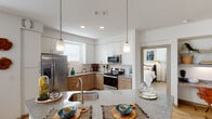 Located in Leander, TX 78641, this single-floor residence offers a thoughtfully designed layout with modern finishes and a cohesive aesthetic throughout. The open-concept kitchen serves as the heart of the home, featuring granite countertops, white upper cabinetry paired with warm wood-toned lower cabinets, white subway tile backsplash, and a full suite of stainless steel appliances including a refrigerator, electric range, and over-the-range microwave. A spacious island with an undermount sink and pendant lighting above makes the kitchen ideal for both meal prep and casual dining. Light hardwood flooring flows through the main living areas, connecting the kitchen to the living and dining spaces. The dining area benefits from ample natural light through multiple windows dressed with blinds and patterned curtains. The living area offers a comfortable, well-lit environment with neutral walls. A light-filled hallway with light wood flooring connects the main living spaces to the bedrooms. The bedrooms are carpeted and include ceiling fans, and the primary bedroom features a walk-in closet. The primary bathroom is well-appointed with dual sinks set in a granite vanity with wood cabinetry, tile flooring, a soaking tub, and a glass-enclosed walk-in shower.