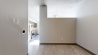 This thoughtfully designed single-floor space offers a contemporary aesthetic defined by clean lines, light wood-tone flooring, and striking exposed concrete ceilings throughout. The open-concept kitchen is a functional centerpiece, equipped with rich warm-toned wood cabinetry, stainless steel appliances including a range, microwave, refrigerator, and dishwasher, a textured tile backsplash, and a peninsula with a sleek countertop. A stacked in-unit washer and dryer is conveniently integrated into the kitchen area. Large windows in the kitchen and living area allow abundant natural light to pour in, offering views of the surrounding building exterior. The living area is bright and open, with light-washed flooring and a neutral color palette that enhances the sense of space. The bedroom is a calm, well-proportioned room featuring a ceiling fan, a reach-in closet with hanging rod, and the same exposed concrete ceiling detail that carries throughout the unit. The bathroom is finished with warm wood cabinetry, a framed mirror, an undermount sink with modern fixtures, and a separate shower enclosure. A smart thermostat is visible in the living area, adding a modern convenience touch. Overall, the space presents a cohesive, urban-modern character with industrial and contemporary design elements working harmoniously together.