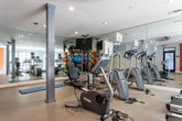 Located in Atlanta, GA (30316), this single-floor fitness center is thoughtfully designed to support a comprehensive workout experience. The space is characterized by a vibrant color palette, featuring bold orange accent walls paired with soft light blue walls, creating an energizing yet balanced atmosphere throughout.

The cardio zone is well-stocked with multiple treadmills and elliptical machines, all positioned to take advantage of large windows that bring in natural light and offer outdoor views. Full-length wall mirrors run the length of the cardio area, enhancing the sense of openness and allowing users to monitor their form during exercise.

A dedicated functional training area features an array of equipment including stability balls, medicine balls, resistance bands, foam rollers, and a stretch mat, making it ideal for cross-training and flexibility work. A mounted flat-screen television is positioned above this section for entertainment during workouts.

The space also includes a stationary bike and additional strength accessories organized on a dedicated rack, ensuring everything is within easy reach. Recessed lighting throughout provides even illumination across all zones. A restroom is accessible directly within the facility, adding convenience for users. Cylindrical support columns accent the layout, contributing to the space's clean, modern aesthetic. The durable speckled flooring ties the entire space together with both practicality and style.