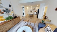 This thoughtfully designed single-floor residence showcases a bright, open-concept layout that effortlessly connects the living, dining, and kitchen areas into one cohesive living space. Light-toned hardwood flooring runs throughout, lending warmth and continuity across every zone.

The kitchen is outfitted with sleek white cabinetry, a subway tile backsplash, stainless steel appliances including a full-size refrigerator, and a central island that doubles as a casual dining and prep space. Open shelving adds a modern, airy touch to the cabinetry arrangement.

The dining area accommodates a mid-sized table and chairs positioned just steps from the kitchen, making it ideal for everyday meals or entertaining. The living area features a neutral, geometric area rug that anchors the seating arrangement, complemented by stylish accent furniture including a geometric-patterned sideboard.

A standout convenience of this residence is the in-unit stacked washer and dryer, discreetly tucked into a dedicated nook, eliminating the need for shared laundry facilities.

Recessed lighting throughout ensures consistent, even illumination, while the clean white walls and minimalist aesthetic create a calm, contemporary ambiance. The overall design prioritizes both functionality and modern style in a compact, efficient footprint.