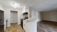 Located at 1700 Hunter Ridge Ln in Peachtree Corners, GA, this single-floor, 3-bedroom, 2-bathroom home offers a practical and well-appointed layout. The kitchen is a standout feature, designed in a galley style with white shaker cabinetry, granite-look countertops, a subway tile backsplash, and black appliances including an electric range and full-size refrigerator. A peninsula with counter seating creates an open connection to the adjacent living and dining area, which is finished with rich, dark wood-style vinyl flooring and track lighting overhead. The textured ceilings are consistent throughout the common areas, adding subtle visual depth. Both bathrooms mirror the kitchen's aesthetic, featuring white vanity cabinetry with granite-look countertops and matching wood-style flooring. The bedrooms are carpeted for comfort and each includes a window with blinds for natural light and privacy. The bedrooms also include closet space with built-in shelving. Neutral warm-beige wall tones create a cohesive and versatile backdrop throughout the home, making it easy to personalize. The floorplan is efficiently organized, offering a comfortable and functional living environment suitable for a variety of lifestyles.