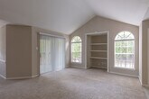 Located at 2330 Montgomery Park Blvd in Conroe, Texas, this single-story residence offers a thoughtfully designed layout with a range of practical features throughout. The living area is a standout space, showcasing soaring vaulted ceilings that create an open, airy atmosphere. Natural light flows in through a prominent arched window, complementing the neutral-toned carpet flooring and a sliding glass door that provides access to an outdoor area. A pass-through opening connects the living space to the kitchen, which is equipped with white cabinetry, granite-style countertops, wood-look flooring, and standard appliances including a full-size refrigerator and dishwasher. The bedrooms are carpeted and well-lit, with one featuring vaulted ceilings, built-in shelving, and a walk-in closet outfitted with wire shelving systems for organized storage. A ceiling fan is present in at least one additional bedroom. The residence includes two bathrooms: one with a granite-topped vanity, a framed mirror, and a shower-tub combination, and a second with a stand-alone walk-in shower and wood-look flooring. Neutral wall tones and consistent finishes throughout give the home a cohesive, functional aesthetic.