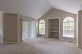 Located at 2330 Montgomery Park Blvd in Conroe, Texas, this single-story residence offers a thoughtfully designed layout with a range of practical features throughout. The living area is a standout space, showcasing soaring vaulted ceilings that create an open, airy atmosphere. Natural light flows in through a prominent arched window, complementing the neutral-toned carpet flooring and a sliding glass door that provides access to an outdoor area. A pass-through opening connects the living space to the kitchen, which is equipped with white cabinetry, granite-style countertops, wood-look flooring, and standard appliances including a full-size refrigerator and dishwasher. The bedrooms are carpeted and well-lit, with one featuring vaulted ceilings, built-in shelving, and a walk-in closet outfitted with wire shelving systems for organized storage. A ceiling fan is present in at least one additional bedroom. The residence includes two bathrooms: one with a granite-topped vanity, a framed mirror, and a shower-tub combination, and a second with a stand-alone walk-in shower and wood-look flooring. Neutral wall tones and consistent finishes throughout give the home a cohesive, functional aesthetic.