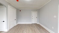 This single-floor unit presents a clean, contemporary aesthetic throughout its thoughtfully arranged layout. The living area is finished with light hardwood-style flooring and neutral gray walls accented by crisp white crown molding and baseboards. A charming arched doorway connects the living space to an adjoining area, adding architectural character while maintaining an open, airy feel. Multiple windows fitted with blinds allow natural light to filter throughout.

The kitchen is efficiently designed and features white shaker-style cabinetry, a white subway tile backsplash, a stainless steel refrigerator, a gas range, and a stainless steel wall-mounted range hood. A single-basin sink with a modern faucet completes the functional workspace.

The bedroom is carpeted in a warm neutral tone, offering a softer contrast to the hard flooring found elsewhere in the unit. Gray walls and white trim carry through consistently, maintaining a cohesive design palette.

The bathroom includes a soaking tub finished with white subway tile surround and dark grout, paired with matte black hardware fixtures, giving it a clean, modern look. A window above the tub provides natural ventilation and light.