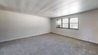 This two-bedroom, one-bathroom residence in Drexel Hill, PA offers a practical and comfortable single-floor layout. The entrance leads into a hallway that connects the living spaces throughout. The spacious living room features soft carpeting, neutral white walls, and windows that invite natural light, creating a bright and airy atmosphere. The kitchen is well-appointed with warm honey-toned wood cabinetry, granite-style countertops, a stone tile backsplash, and black appliances including a gas range, built-in microwave, and dishwasher, all set on clean tile flooring. The generously sized primary bedroom offers plush carpeting, a dedicated closet with built-in shelving, and a window with outdoor views. The second bedroom is similarly carpeted with neutral tones, its own window, and baseboard heating. Both bedrooms provide a calm, understated setting. The bathroom is a standout with retro-inspired mint green ceramic tile walls accented by a dark border, a classic soaking tub, and a mosaic tile floor. With four closets spread throughout the unit, storage is ample. The overall ambiance is clean, neutral, and move-in ready.