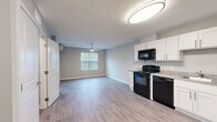 This efficient yet thoughtfully designed single-story unit offers a comfortable layout encompassing a kitchen, living room, bedroom, bathroom, closet, and hallway. The open-concept main area seamlessly connects the kitchen and living room, creating a cohesive and functional living space. Light gray walls and durable luxury vinyl plank flooring run throughout, lending a clean, contemporary aesthetic.

The kitchen is well-equipped with full black appliances — including a refrigerator, electric range, over-the-range microwave, and dishwasher — set against crisp white shaker-style cabinetry and light countertops. A ceiling-mounted flush light fixture illuminates the space.

The living area benefits from a large window that brings in natural light and is fitted with a ceiling fan for added comfort. The bedroom is a comfortable size, featuring its own ceiling fan, a wall-mounted mini-split HVAC unit, and a window with blinds. A dedicated walk-in closet with wire shelving provides practical storage.

The bathroom includes tile flooring, a vanity with white cabinetry, and clean neutral-toned walls. Throughout the unit, white trim and panel-style doors contribute to a polished, modern finish, making this a well-organized and move-in-ready space.