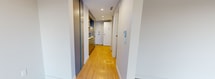 This efficiently designed single-floor unit offers a well-organized layout accommodating two kitchen areas, a living room, one bathroom, and a dedicated laundry space within a compact footprint. The interior presents a clean, contemporary aesthetic, characterized by light wood-effect flooring, neutral cream-toned walls, and recessed ceiling details that add subtle architectural interest throughout.

The living room is notably bright, benefiting from a large floor-to-ceiling sliding glass door and adjacent window that frame views of surrounding greenery and provide direct access to a private outdoor patio. The patio, accessible via a glass-paneled entrance door, offers an outdoor extension of the living space with stone tile flooring.

The kitchen features a streamlined, modern design with flat-front grey cabinetry, white countertops, a stainless steel sink with a contemporary pull-down faucet, an induction cooktop, under-cabinet lighting, and overhead stainless steel range hood, complemented by upper cabinetry extending to the ceiling for maximum storage.

The bathroom is finished with large-format tile flooring, a floating grey vanity with a white basin, a full-width mirror, and a soaking bathtub with tiled surround. A separate laundry room with wood-effect flooring and built-in hookups completes the functional layout of this neatly appointed space.