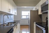Located at 2077 Prospect St in Burlington, Ontario, this one-bedroom, one-bathroom unit offers a well-organized layout across a single floor. The open-concept living, dining, and kitchen area forms the heart of the space, bathed in natural light from large sliding doors that lead directly to a private balcony with outdoor views of the surrounding neighbourhood. The parquet wood flooring throughout the living and bedroom areas adds warmth and character to the clean, white-walled interior.

The galley-style kitchen is efficiently designed with white shaker cabinetry, dark countertops, a stainless steel undermount sink, and a full suite of stainless steel appliances including a refrigerator, electric range, and built-in microwave. Track lighting overhead ensures excellent task illumination. Light-toned ceramic tile flooring completes the kitchen's crisp, modern aesthetic.

The bedroom is a comfortable and quiet retreat, featuring the same warm parquet flooring, a closet, and a broad window that frames outdoor views and allows ample natural light to enter. A baseboard heating unit runs along the wall beneath the window.

The bathroom is finished with classic cream subway tile surrounding a full soaking tub and shower combination, accented with polished chrome fixtures for a clean, timeless look.