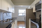 Located at 2077 Prospect St in Burlington, Ontario, this one-bedroom, one-bathroom unit offers a well-organized layout across a single floor. The open-concept living, dining, and kitchen area forms the heart of the space, bathed in natural light from large sliding doors that lead directly to a private balcony with outdoor views of the surrounding neighbourhood. The parquet wood flooring throughout the living and bedroom areas adds warmth and character to the clean, white-walled interior.

The galley-style kitchen is efficiently designed with white shaker cabinetry, dark countertops, a stainless steel undermount sink, and a full suite of stainless steel appliances including a refrigerator, electric range, and built-in microwave. Track lighting overhead ensures excellent task illumination. Light-toned ceramic tile flooring completes the kitchen's crisp, modern aesthetic.

The bedroom is a comfortable and quiet retreat, featuring the same warm parquet flooring, a closet, and a broad window that frames outdoor views and allows ample natural light to enter. A baseboard heating unit runs along the wall beneath the window.

The bathroom is finished with classic cream subway tile surrounding a full soaking tub and shower combination, accented with polished chrome fixtures for a clean, timeless look.