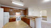 Located at 100 Wesley Stonecrest Circle in Stonecrest, GA, this single-floor, 2-bedroom, 2-bathroom residence offers a well-organized layout designed for comfortable everyday living. The kitchen is equipped with warm honey-toned wood cabinetry, a tile backsplash, laminate countertops, a double-basin sink, and white appliances including an electric range and dishwasher. A pass-through opening connects the kitchen to the living and dining area, enhancing the open flow of the space. The combined living and dining room features elegant crown molding, a tray ceiling with a ceiling fan, wainscoting detail, a decorative pendant light, and a glass-panel door flanked by windows that invite abundant natural light and outdoor views. Both bedrooms are carpeted and offer a calm, neutral palette, with the primary bedroom providing a generous footprint and direct views of the surrounding community. Each of the two bathrooms includes a tub-shower combination with white tile accented by a black diamond tile border, a wood-vanity with a single sink, and tile flooring. Additional spaces include a pantry, entrance, and hallway, contributing to the home's practical and functional design throughout.