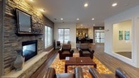This well-appointed single-floor clubhouse offers a thoughtfully designed collection of amenity spaces ideal for both relaxation and productivity. The centerpiece of the space is a spacious lounge area anchored by a floor-to-ceiling stacked stone fireplace flanked by large windows that invite natural light. Plush leather armchairs arranged around a wood coffee table on a vibrant geometric rug create a warm, inviting atmosphere.

Adjacent to the lounge, a café-style coffee bar features a sleek dark-cabineted island with a white countertop, pendant lighting, and bar seating. A microwave and additional counter space round out the café setup, while a sliding glass door leads directly to an outdoor patio area. Coffee-themed artwork adds a playful, welcoming touch.

A dedicated fitness center, visible through large glass panels, is equipped with treadmills and mirrors, offering an open and motivating workout environment. Nearby, a comfortable reading nook with leather armchairs and a small bookshelf provides a quiet retreat.

The space also includes a professional conference room outfitted with a large boardroom table, ergonomic seating, a wall-mounted flat-screen display, and tasteful botanical artwork. A business center with computer workstations and a collaborative work table rounds out the functional offerings. Rich hardwood-style flooring flows throughout, unifying the space with a polished, cohesive aesthetic.