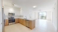Located at 1645 NW 18th St in Miami, FL, this single-floor residence offers a clean, modern design throughout. The open-concept living and kitchen area is anchored by a sleek peninsula with white quartz countertops, an undermount sink, and stainless steel appliances including a refrigerator, electric range, microwave, and dishwasher. The kitchen features two-tone cabinetry with warm wood lower cabinets, white upper cabinets, and a classic subway tile backsplash. Large-format light tile flooring runs throughout the entire unit, contributing to a bright, cohesive aesthetic. The living area extends toward floor-to-ceiling sliding glass doors that open to a private balcony with views of the Miami skyline. Ceiling fans provide comfort in both the living area and bedrooms. The bedrooms are well-proportioned with neutral walls and generous natural light. Each features a spacious walk-in closet with built-in shelving and hanging rods for ample storage. The bathrooms are finished with warm wood vanities, white quartz countertops, backlit mirrors, and tiled shower enclosures. An in-unit washer and dryer area adds everyday convenience. The overall design emphasizes clean lines, neutral tones, and functional living in the heart of Miami.
