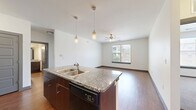 This 2-bedroom, 2-bathroom residence is thoughtfully designed to maximize both comfort and functionality across a single floor. The open-concept kitchen and living area serves as the heart of the home, featuring a central island with granite countertops, a double stainless steel sink, and pendant lighting overhead. The kitchen is equipped with dark wood cabinetry on the lower level, gray upper cabinets, a tile backsplash, and black appliances including a range, microwave, and refrigerator. Rich hardwood-style flooring extends throughout the main living areas, while a ceiling fan and a window admitting natural light complete the living room. The primary bedroom features hardwood-style flooring, a ceiling fan, and a window with exterior views, while the second bedroom is carpeted and similarly benefits from natural light and a ceiling fan. Each bedroom is served by a dedicated closet. The two bathrooms are finished with large-format gray wall tile surrounding soaking tubs, dark wood vanity cabinetry, granite countertops, and hardwood-style flooring. The overall aesthetic is modern and neutral, with clean white walls and dark trim accents creating a cohesive, contemporary ambiance throughout.