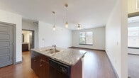 This 2-bedroom, 2-bathroom residence is thoughtfully designed to maximize both comfort and functionality across a single floor. The open-concept kitchen and living area serves as the heart of the home, featuring a central island with granite countertops, a double stainless steel sink, and pendant lighting overhead. The kitchen is equipped with dark wood cabinetry on the lower level, gray upper cabinets, a tile backsplash, and black appliances including a range, microwave, and refrigerator. Rich hardwood-style flooring extends throughout the main living areas, while a ceiling fan and a window admitting natural light complete the living room. The primary bedroom features hardwood-style flooring, a ceiling fan, and a window with exterior views, while the second bedroom is carpeted and similarly benefits from natural light and a ceiling fan. Each bedroom is served by a dedicated closet. The two bathrooms are finished with large-format gray wall tile surrounding soaking tubs, dark wood vanity cabinetry, granite countertops, and hardwood-style flooring. The overall aesthetic is modern and neutral, with clean white walls and dark trim accents creating a cohesive, contemporary ambiance throughout.