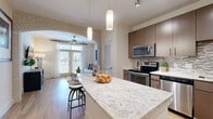 Located at 5880 Inwood Dr in Houston's desirable Galleria corridor, this thoughtfully designed one-bedroom, one-bathroom residence offers a cohesive open-concept layout across a single floor. The kitchen is a standout feature, boasting rich dark-walnut cabinetry, a mosaic tile backsplash, stainless steel appliances including a range, microwave, dishwasher, and refrigerator, and a generous granite-topped island with bar seating beneath elegant pendant lighting — ideal for casual dining or entertaining. Light wood-style flooring flows throughout the main living areas, lending warmth and continuity. The living room is framed by a decorative stone archway and French doors that invite natural light and provide outdoor access, complemented by a ceiling fan overhead. The spacious bedroom features plush carpeting, dual windows with sheer curtains offering ample natural light, and an open closet for convenient storage. The bathroom is finished with large-format tile walls, a glass-enclosed walk-in shower, and modern cabinetry for storage. A connecting hallway ties the layout together efficiently. The overall ambiance is modern and comfortable, with clean lines and neutral tones creating a welcoming atmosphere throughout.