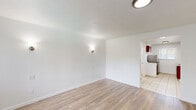 Located at 300 E Foothill Blvd in Pomona, California, this single-floor unit offers a practical and efficient layout comprising a living room, kitchen, bathroom, and closet. The living room greets you upon entry with light wood-tone laminate flooring, crisp white walls, and a front-facing window fitted with vertical blinds that allow natural light to filter in. A wall-mounted HVAC unit provides climate control, and wall sconces add ambient lighting throughout the space. The kitchen features rich, dark wood cabinetry — both upper and lower — paired with a granite-style countertop, a stainless steel sink, a gas range, and a full-size refrigerator. Light ceramic tile flooring and a window above the sink area contribute to a clean, functional workspace. The bathroom includes a full tub and shower combination, a toilet, and a vanity with a sink, finished with light tile flooring and neutral wall surrounds. A dedicated closet provides essential storage. The overall aesthetic is clean and minimalist, with white walls throughout creating a bright, neutral canvas. The space is well-suited for single occupancy, offering all essential amenities in a compact, efficiently organized footprint.