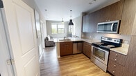 Located at 303 W Blount Ave in Knoxville, TN, this one-bedroom, one-bathroom unit offers a well-designed layout across a single floor. The open-concept kitchen flows seamlessly into the living area, creating a cohesive and functional space. The kitchen is outfitted with dark wood-grain cabinetry, granite-style countertops, a peninsula with a built-in sink, and a full suite of stainless steel appliances including a refrigerator, electric range, over-the-range microwave, and dishwasher. Light hardwood-style flooring and pendant lighting add a modern touch throughout the kitchen and living areas. The living room benefits from multiple windows that invite generous natural light and offer views of the surrounding neighborhood and greenery. A ceiling fan provides additional comfort. The bedroom is a comfortable, carpeted retreat with its own ceiling fan, a window framing outdoor views, and direct access to a walk-in closet equipped with wire shelving for organized storage. The bathroom features tile flooring, a wood-grain vanity with a clean white countertop, and convenient access to the walk-in closet. Neutral gray wall tones and clean white trim throughout give the unit a cohesive, contemporary aesthetic.